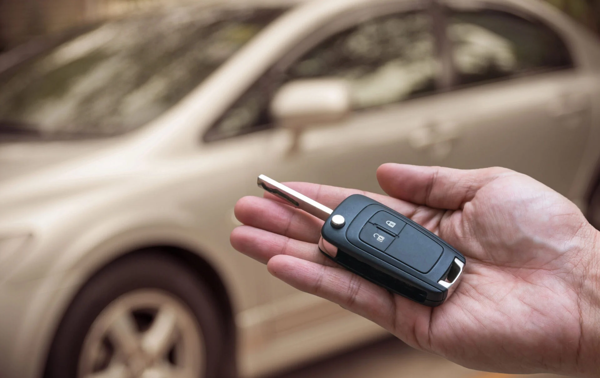 person holding key fob in palm in front of car