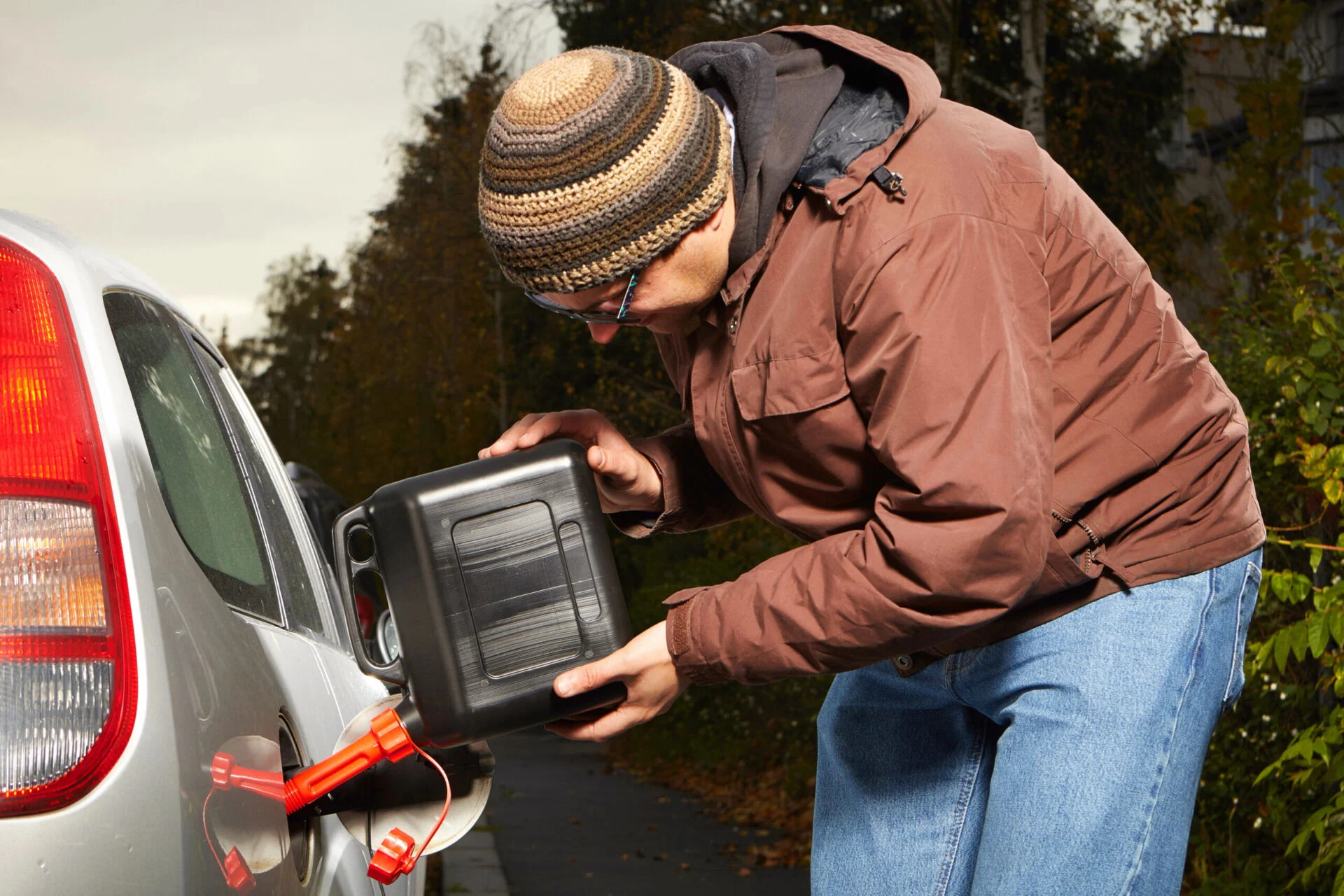 Man fills vehicle gas tank from a small container