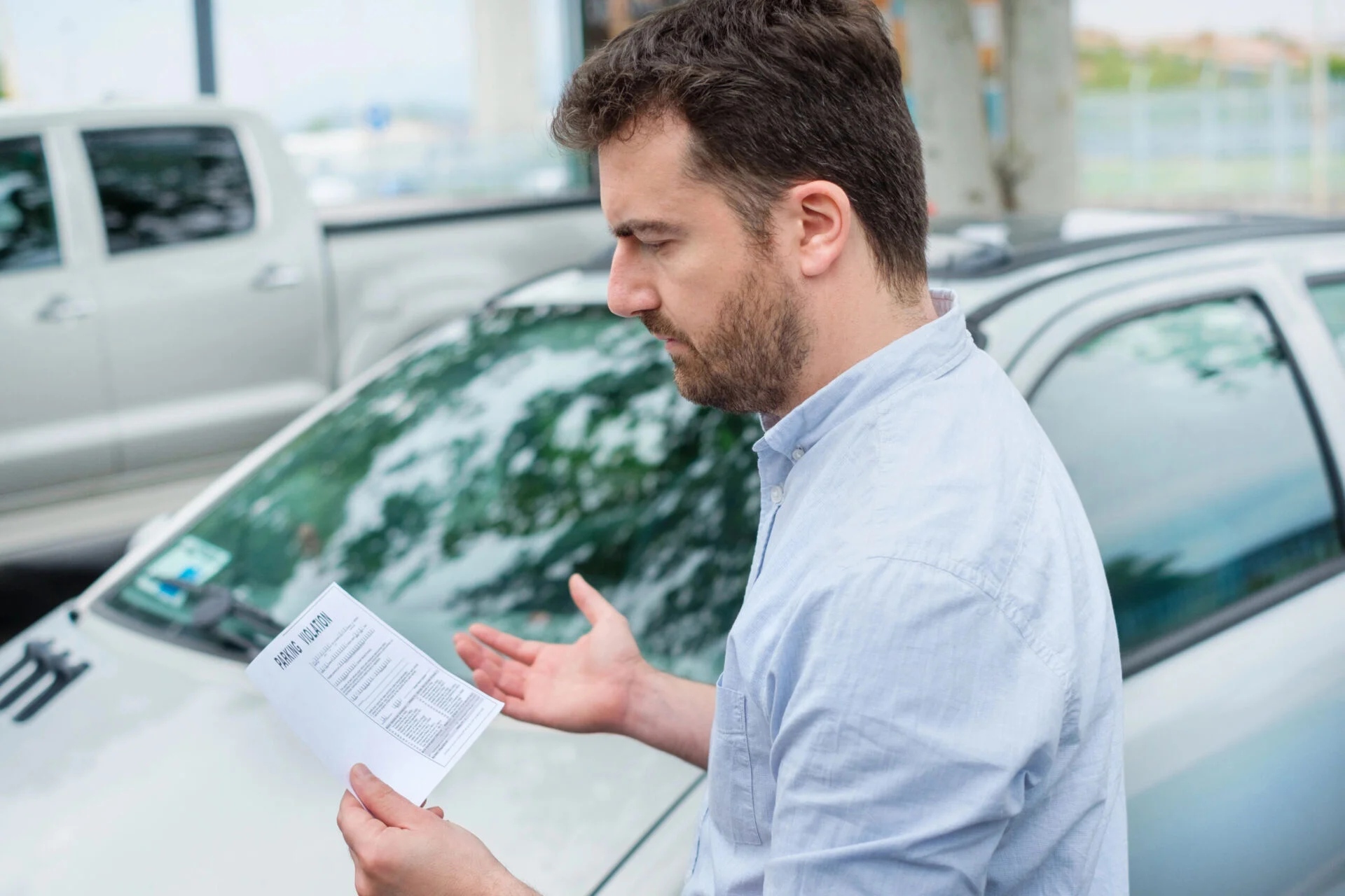 Man looks confused as he looks at a parking ticket while standing next to his car