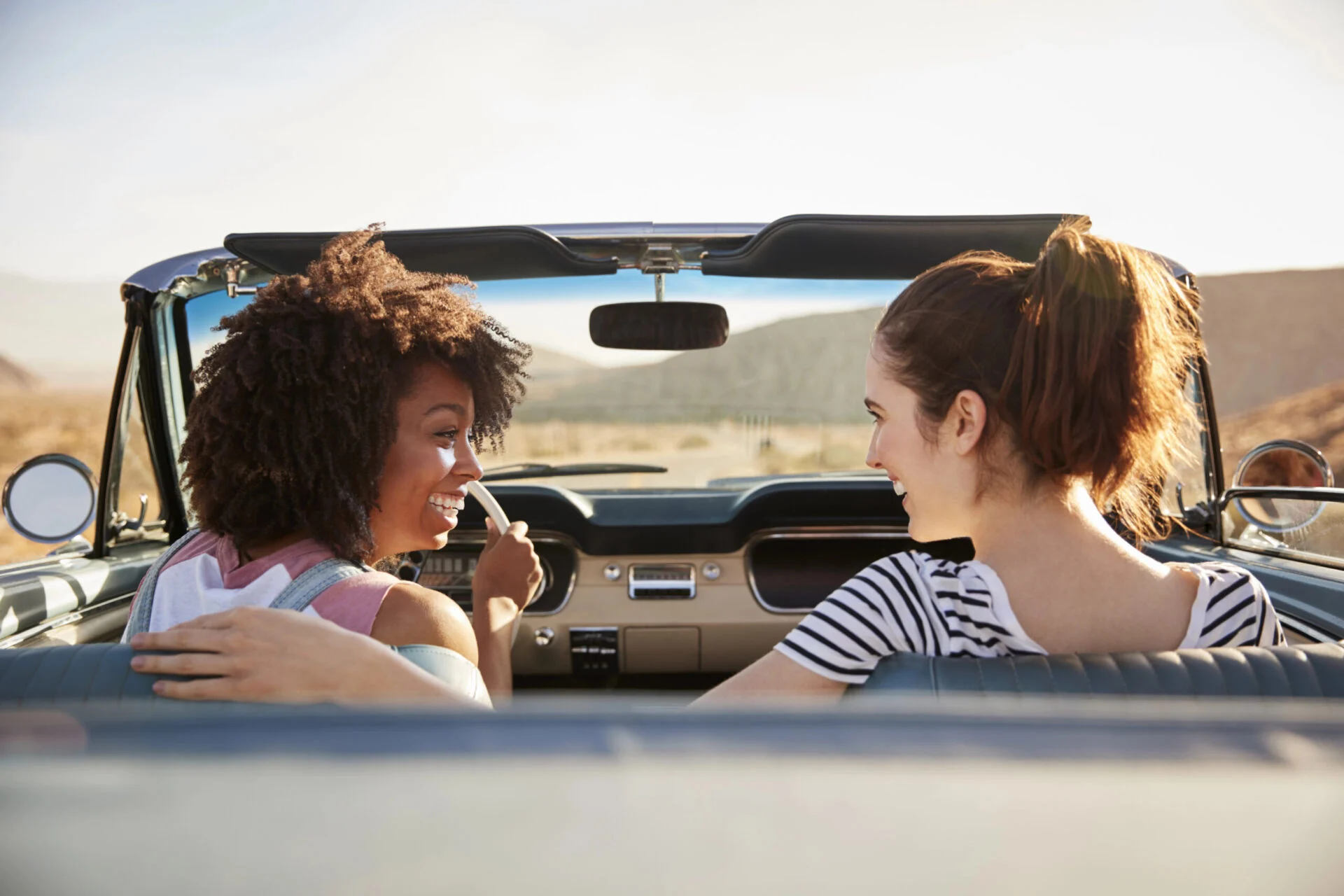 Two teens driving in California in a convertible car