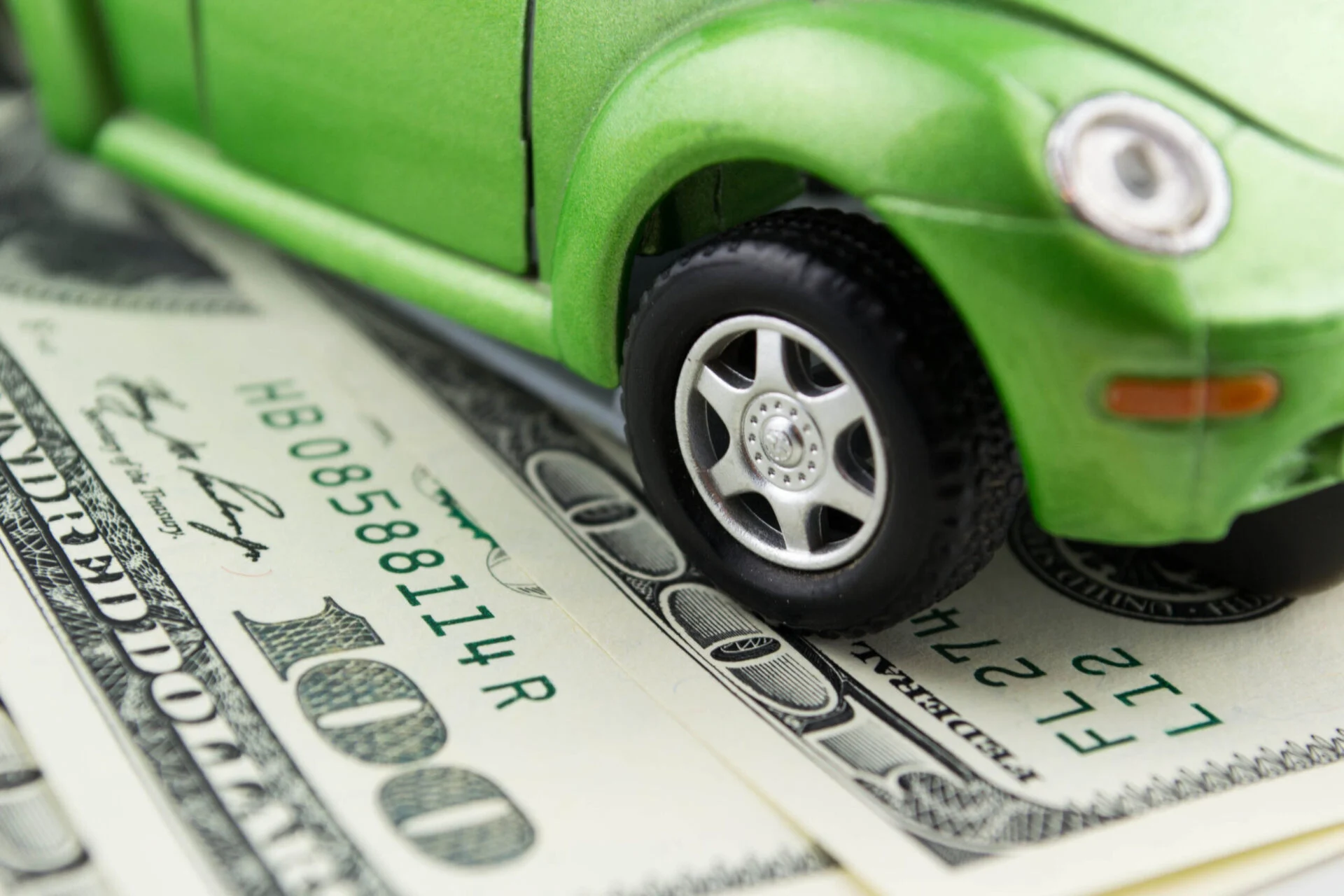 Green toy car sits on top of $100 bills