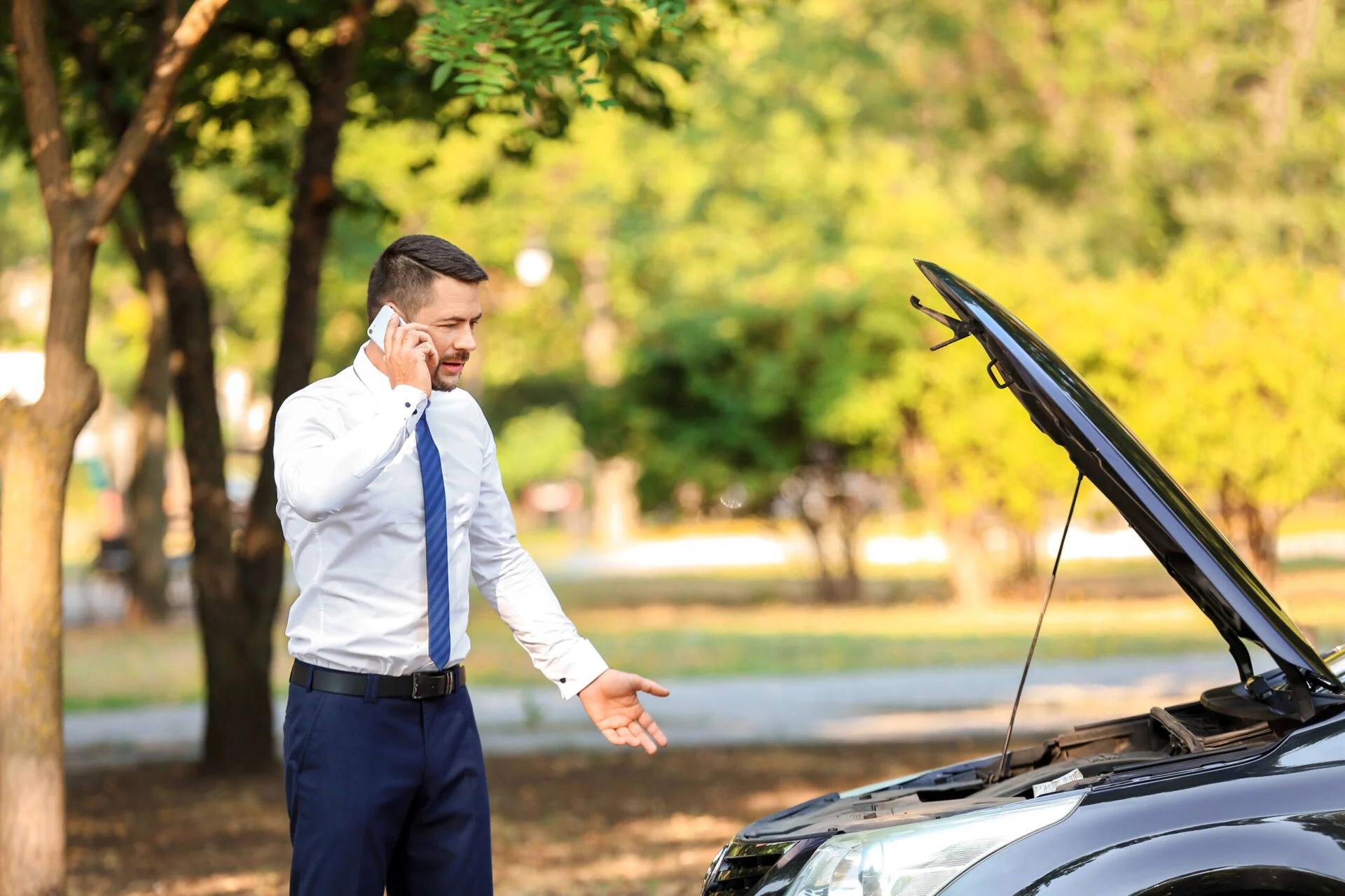 Man on the phone will checking under the hood of car