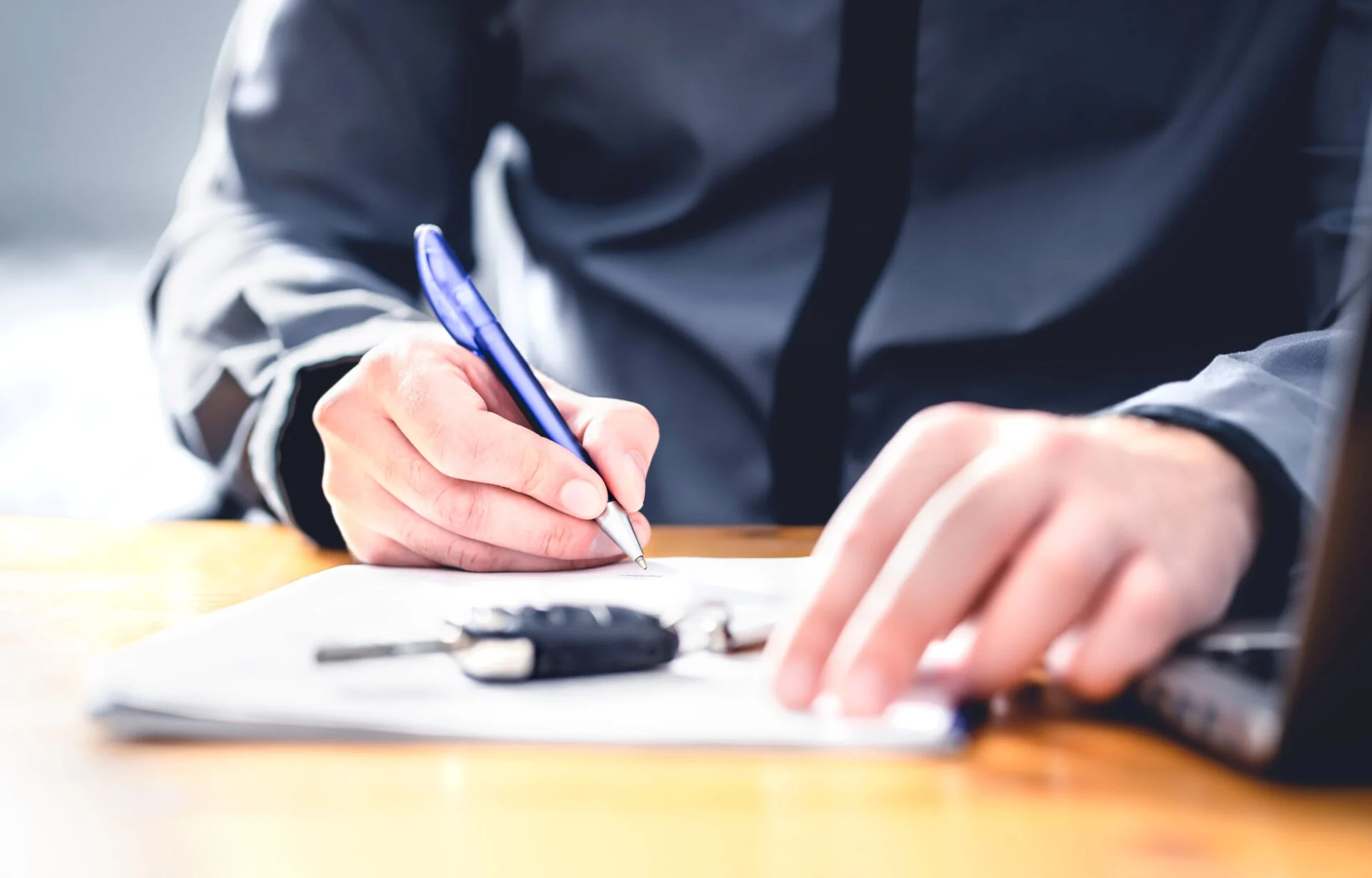 Person signing paper with car keys on table.