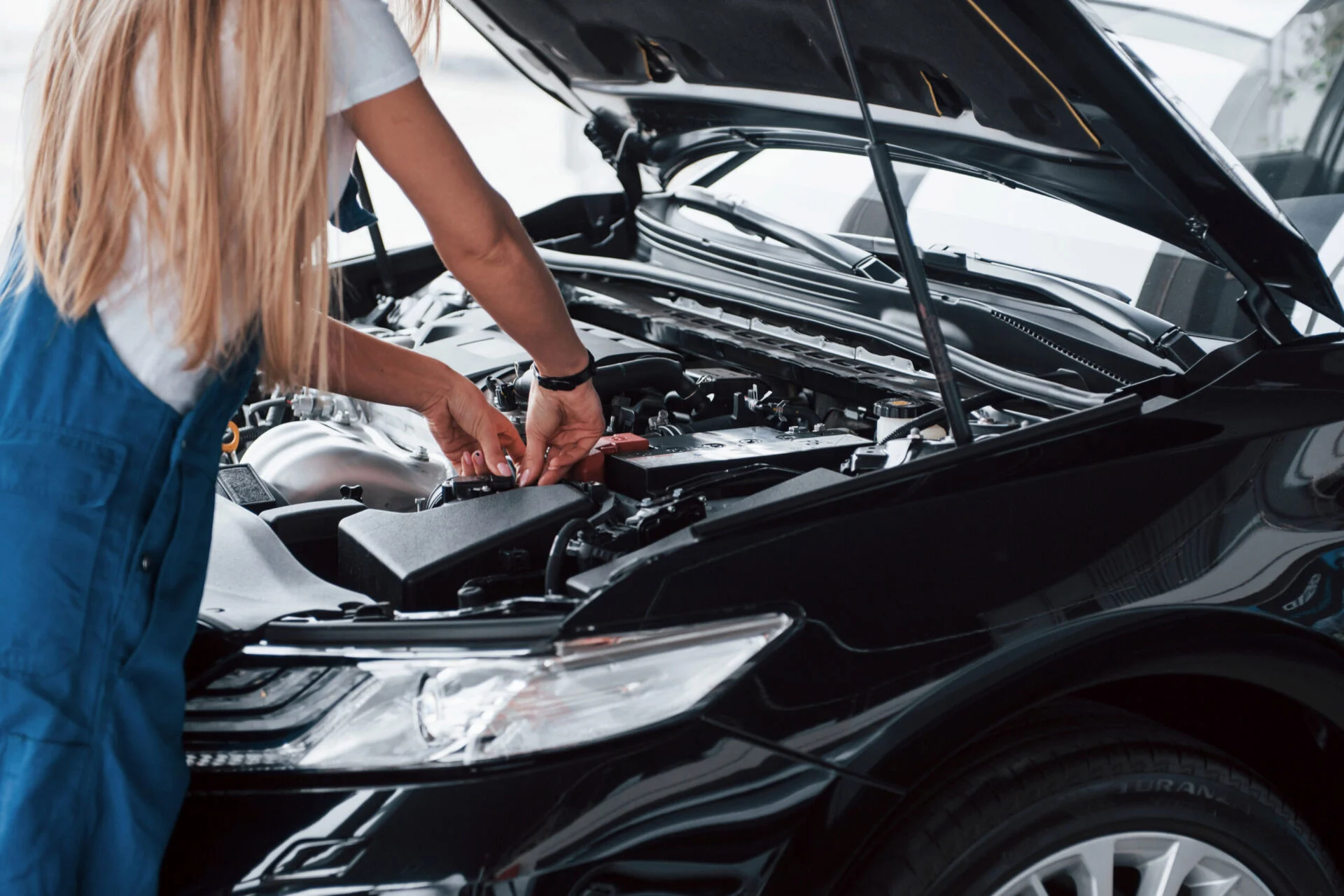 Female works on car engine with the hood popped
