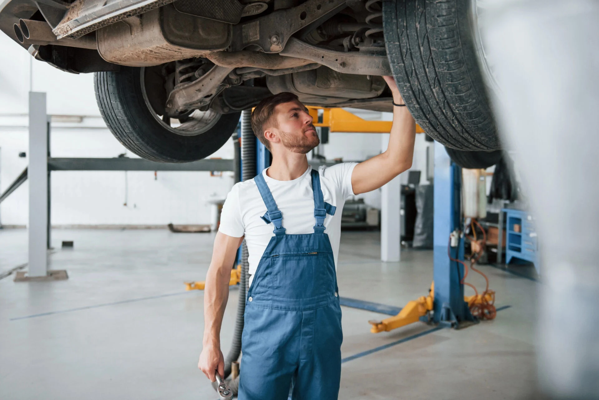 Mechanic in blue overalls checking the undercarriage of a car.