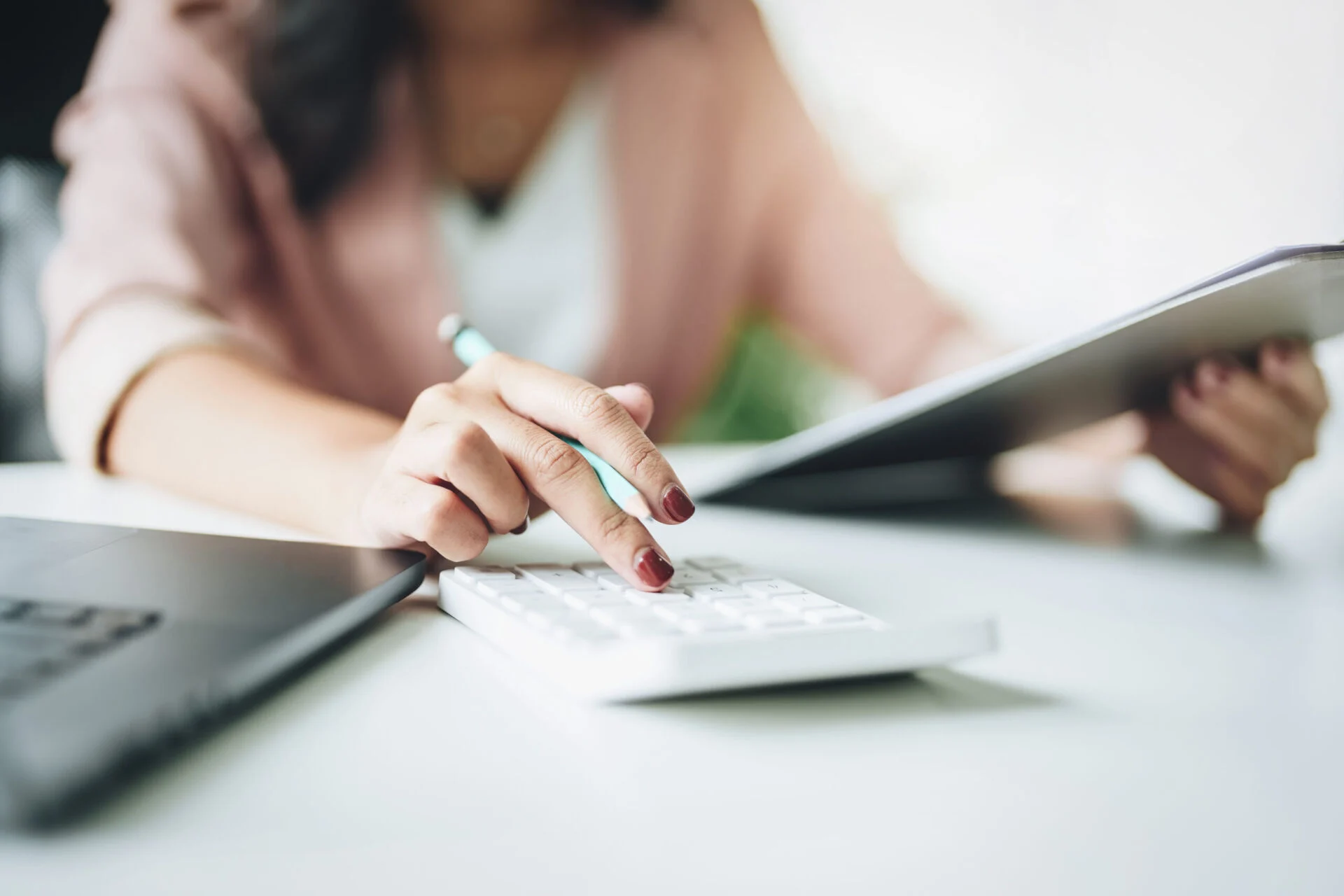 Close-up of woman's hands using calculator and laptop.