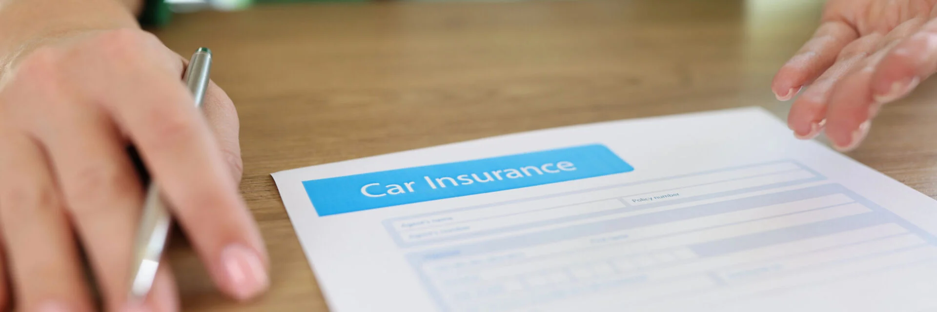 Car insurance paperwork on a desk with a person holding a pen