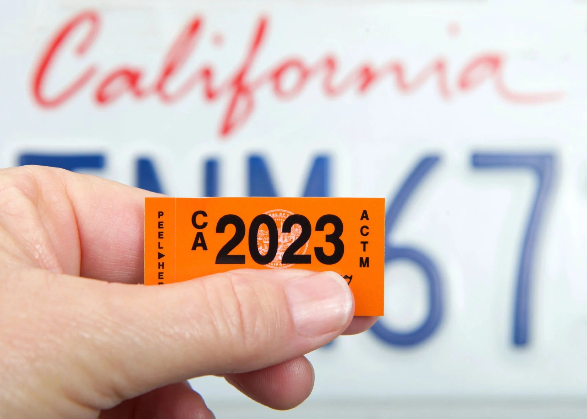 A person holding a license plate sticker for the state of California that expires in 2023