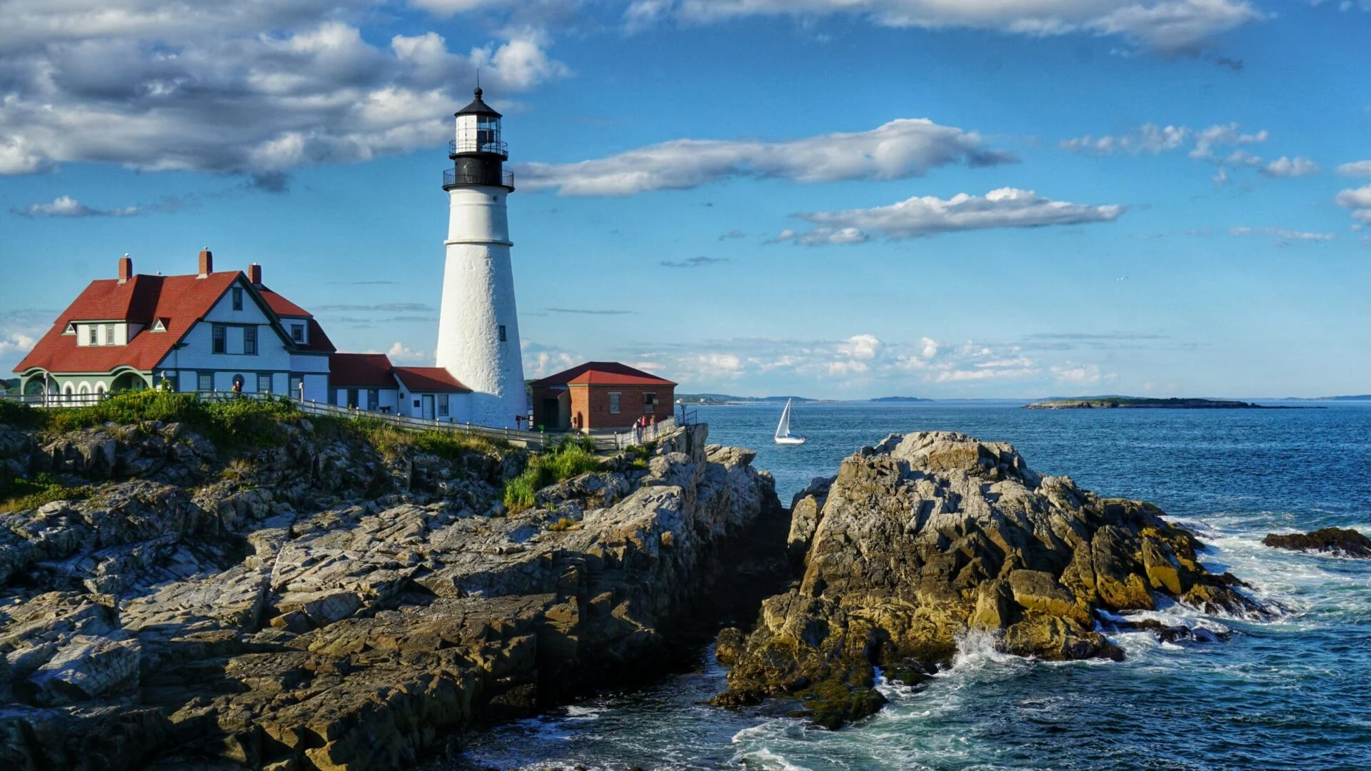 Popular Portland Head Light Lighthouse in Maine with sailboat and blue sky
