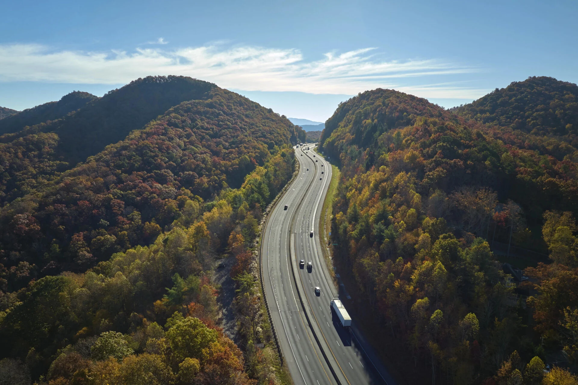 Aerial view of I-40 freeway in North Carolina heading to Asheville through Appalachian mountains in golden fall with moving trucks and cars. Interstate transportation concept.